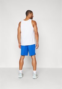 Hvit nett tanktopp og blå treningsshorts. Tanktoppen har en avrundet halslinje; shortsen har sidelister og en jevn tekstur.