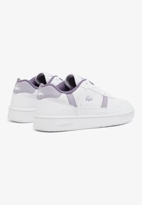 Sneakers Lacoste blancs avec des accents violets, dotés d'une tige en synthétique lisse, d'un détail perforé sur le côté et d'une semelle en caoutchouc. Design minimaliste.
