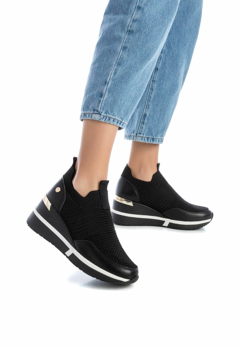 Zapatillas de cuña negras de punto con tejido texturizado, laterales elásticos y un acabado negro liso con acentos metálicos en el tacón. Detalles en la suela blanca.