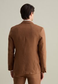 Giacca di lino marrone con colletto a punta, fessura posteriore singola e polsi con bottoni. Tessuto liscio e vestibilità su misura.