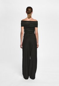 Svart off-shoulder topp med plisserad detalj, parat med högmidjade, vida svarta byxor. Slät textur och figursydd silhuett.