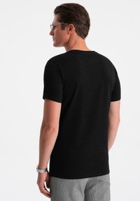 Sort bomulds t-shirt med korte ærmer, rund halsudskæring, glat tekstur, båret af en person set bagfra, parret med grå ternede bukser.