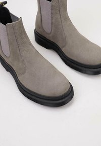 Harmaat mokkanahka Chelsea-saappaat pyöristetyllä varvaskärjellä, mustalla kumipohjalla ja elastisilla sivupaneeleilla helpompaa pukemista varten. Sujuva pinta, jossa on minimaalinen ommel.