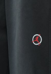 Μαύρο αθλητικό παντελόνι με μαλακή υφή, με κόκκινο και λευκό κυκλικό λογότυπο που απεικονίζει τη σιλουέτα ενός καλαθοσφαιριστή.