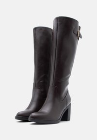 Botas altas hasta la rodilla de cuero liso marrón, con tacón ancho, cremallera lateral y detalle decorativo de correa con hebilla.