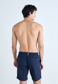 Mørkeblå badebukser med elastisk linning, sidelommer og baklomme. Lett stoff med en glatt tekstur.