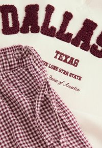 Bordowy sweter z okrągłym dekoltem z teksturowanym napisem "DALLAS", z tkaniną w kratę w kolorze bordowym i białym na dole.