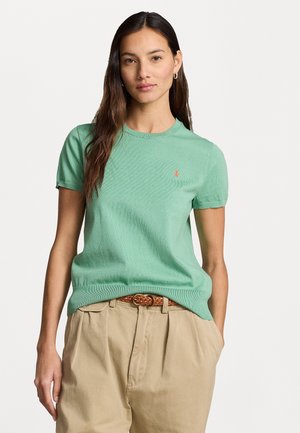 Light green short-sleeve knitted sweater with a crew neckline, featuring a small red logo on the chest, paired with beige high-waisted pants.