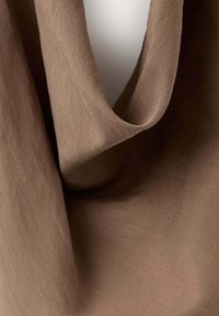 Tissu en lin marron doux drapé pour former une boucle lâche avec une texture visible et des plis naturels sur un fond neutre.