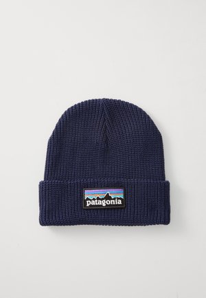 Bonnet en tricot bleu marine avec un revers et une étiquette patch multicolore représentant des montagnes et le nom de marque "Patagonia".