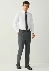 Biela košeľa na gombíky, tmavozelená kravata s bodkami, sivé nohavice s tenkými prúžkami, čierny opasok a čierne šnurovacie topánky. Profesionálny outfit.