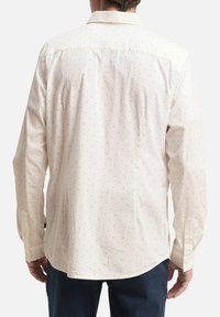 Helle beige Langarmbluse mit kleinen geometrischen Mustern, Knopfkragen und Knopfmanschetten, mit einem lässigen Schnitt und geradem Saum.