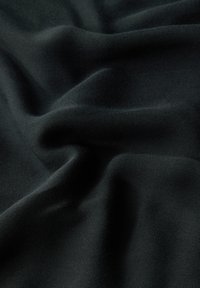 Tissu noir avec une texture lisse, présentant des plis et des ondulations douces. Le matériau semble léger et modérément extensible.