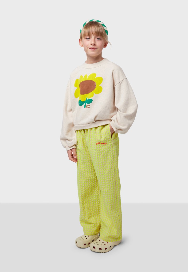 Cream sweatshirt with yellow sunflower graphic, paired with green patterned pants and beige clogs. Features loose fit and soft texture.