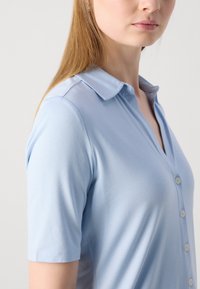 Polo bleu clair avec un col, des manches courtes et un devant à boutons. Texture de tissu lisse et coupe ajustée.