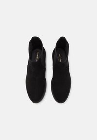 Černé semišové kotníkové boty s hladkým povrchem, elastickými bočními panely a gumovými podrážkami, které se vyznačují minimalistickým designem. Zlatý branding na stélce.