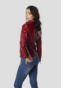 Červená kožená bunda s priliehavým strihom, zdobená detailmi na ramenách a na zips. Nosená s modrými džínsami s kvetinovou výšivkou.