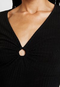 Svart ribbad topp med V-hals, samlat tyg med en cirkulär utskärning i mitten och en texturerad yta.