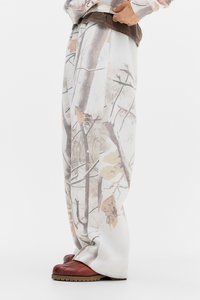 Pantalones de pierna ancha con estampado de camuflaje marrón y blanco, confeccionados en tela suave, con una cinturilla marrón contrastante y un ajuste relajado y texturizado.