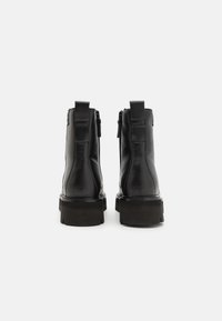 Bottines noires en cuir brillant, avec une fermeture éclair sur le côté, une languette à l'arrière et une semelle en caoutchouc épaisse.