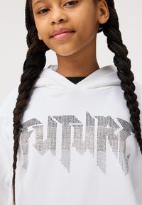 Sweat à capuche blanc avec "FUTURE" en embellissements de strass dégradés. Tissu doux, design à capuche, et accents noirs autour du cou.