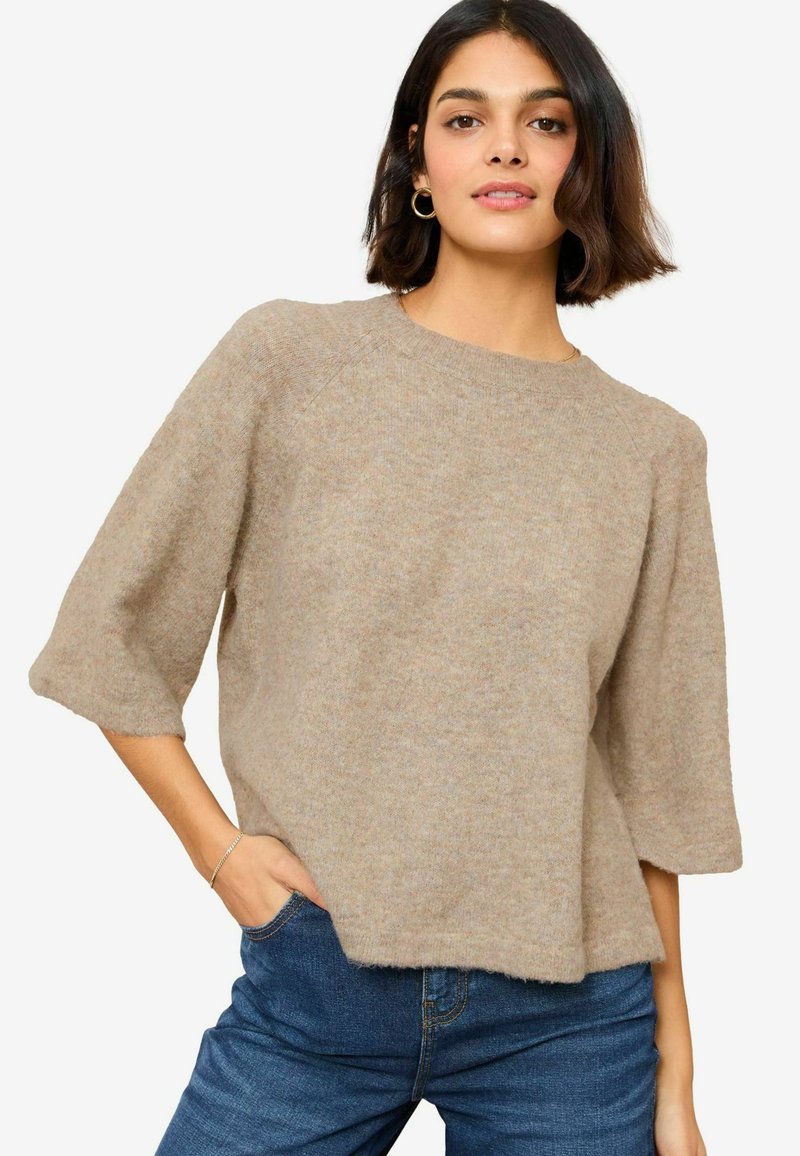 Hellbrauner Strickpullover, Rundhals, kurze Raglanärmel, lockere Passform, strukturierter Stoff, kombiniert mit blauen Jeans.