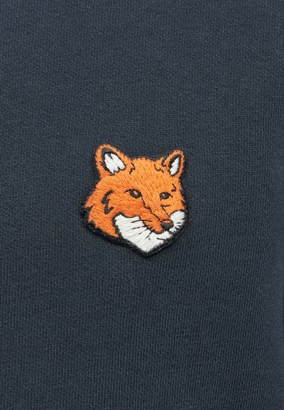 Tessuto blu scuro con una patch ricamata a texture di testa di volpe in arancione e bianco, dotata di dettagli espressivi e bordi delineati.