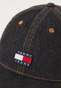 Casquette de baseball en denim bleu foncé avec des coutures orange, ornée d'un patch rectangulaire "TOMMY JEANS" en marine, blanc et rouge. Visière arrondie.
