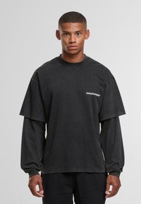 Czarna, oversize koszulka z krótkimi rękawami, nakładana na długie rękawy. Posiada logo na klatce piersiowej i luźny krój. Wykonana z bawełny z teksturowanym wykończeniem.