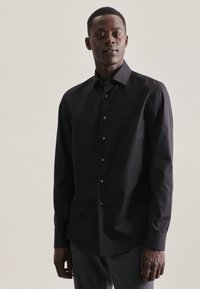 Chemise noire à manches longues, devant boutonné, en tissu lisse, coupe ajustée, ourlet courbé, col classique et accents de boutons discrets.