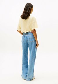 T-shirt giallo accorciata abbinata a jeans a vita alta blu chiaro con gamba larga, caratterizzati da una classica texture in denim e design a cinque tasche.