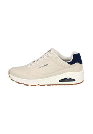 Zapatilla beige Skechers con suela blanca, cojín de aire en el talón, detalles perforados, acento azul marino en el talón y cordones blancos.