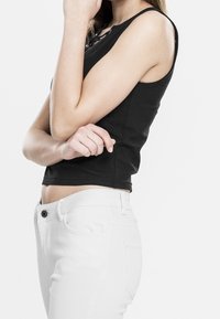 Černý bezramínkový top s kulatým výstřihem, přiléhavý střih. V kombinaci s bílými kalhotami s předními kapsami a zapínáním na knoflík.