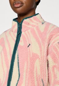 Ζακέτα από μάλλινο ύφασμα σε ροζ, κρεμ και τιρκουάζ με ψηλό γιακά, κλείσιμο με φερμουάρ και αφηρημέ νο μοτίβο· διαθέτει υφή υφάσματος και λεπτομέρεια με λογότυπο.