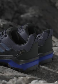 Čierne a námornícke turistické topánky s textúrovaným zvrškom, štítkom GORE-TEX a modrým akcentom na podrážke. Navrhnuté pre odolnosť a trakciu.