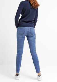 Dünne Jeans aus mittlerem blauen Denim mit einer mittelhohen Taille, gestickten Gesäßtaschen und einer enganliegenden Silhouette, kombiniert mit weißen Sneakers.