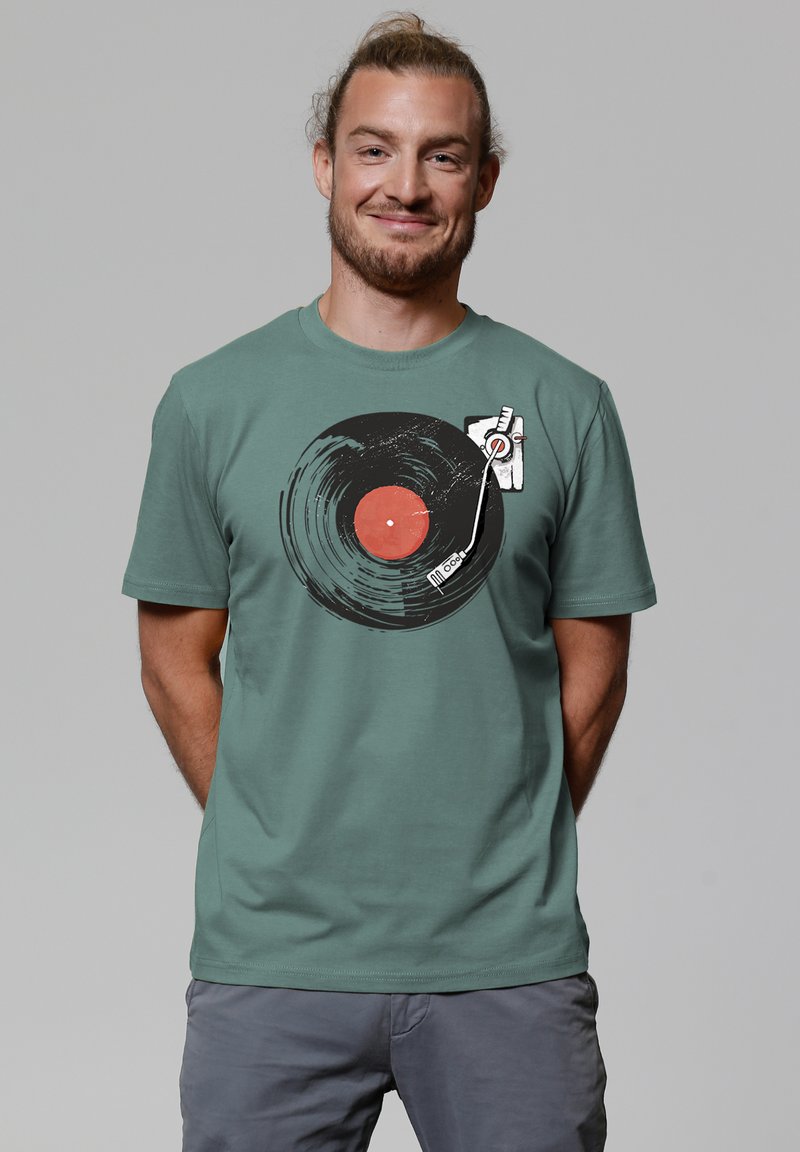 Grünes Baumwoll-T-Shirt mit einem großen, kreisförmigen schwarzen Schallplattengrafik mit rotem Zentrum und einem Plattenspieler-Tonabnehmer.