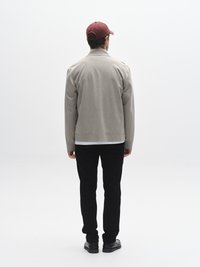 Jachetă cu gulere de culoare gri deschis, pantaloni negri și pantofi închiși la culoare. Șapcă roșie de baseball, textură netedă, design minimalist, fără modele vizibile.