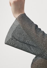 Tessuto nero trasparente intrecciato con fili metallici argentei. Presenta una manica a campana con una texture liscia e bordi puliti.