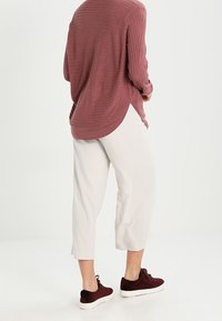 Rippentop in Maroon mit langen Ärmeln, cremefarbene cropped Hose und burgunderrote Sneaker mit weißen Sohlen. Fokus auf Komfort und lässigem Stil.