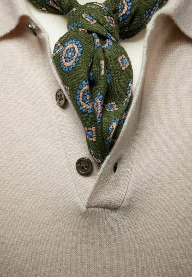 Beige strikket polo skjorte med en tre-knaps placket, prydet med et grønt mønstret tørklæde bundet om halsen. Tørklædet har blå og beige cirkulære mønstre.