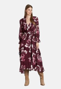Abito maxi floreale in un profondo bordeaux con pattern floreali bianchi e rosa. Presenta maniche a volant, una cintura in vita e un orlo a balze.