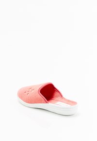 Zapatilla de color coral con tejido suave y texturizado, diseño de parte trasera abierta y suela de goma blanca. Presenta detalles en relieve en la parte superior.