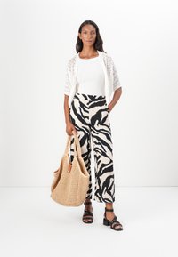Cardigan en tricot blanc, pantalon ample à rayures zèbres noir et blanc, sandales à talons noires et sac fourre-tout tissé beige.