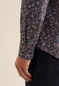 Bloemig patroon shirt in donkere tinten, met kleine blauwe, roze en witte bloemen. Mouwen met manchet en knopen, gemaakt van lichtgewicht stof.