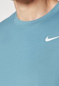 Detailní záběr na osobu, která má na sobě světle modré tričko Nike s bílým logem Nike swoosh na horní části hrudi.
