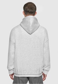 Haut à capuche gris clair avec un cordon de serrage. Le tissu semble doux, avec une coupe décontractée et des poignets et un ourlet côtelés. Pas de logos visibles.