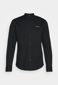 Camicia nera a maniche lunghe con colletto a band, realizzata in tessuto liscio. Presenta bottoni frontali e un ricamo discreto del logo sul petto.