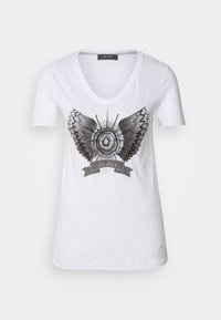 Vit bomullströja med en metallisk grafisk design av vingar och cirkulära mönster med en banner nedanför. V-ringning och korta ärmar.