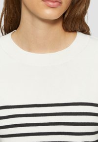 Weißer Strickpullover mit breiten schwarzen horizontalen Streifen. Besitzt einen runden Ausschnitt und eine weiche Textur, geeignet für die legere Kleidung.
